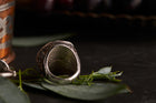 Silver ring with intricate design on a dark surface with leaves