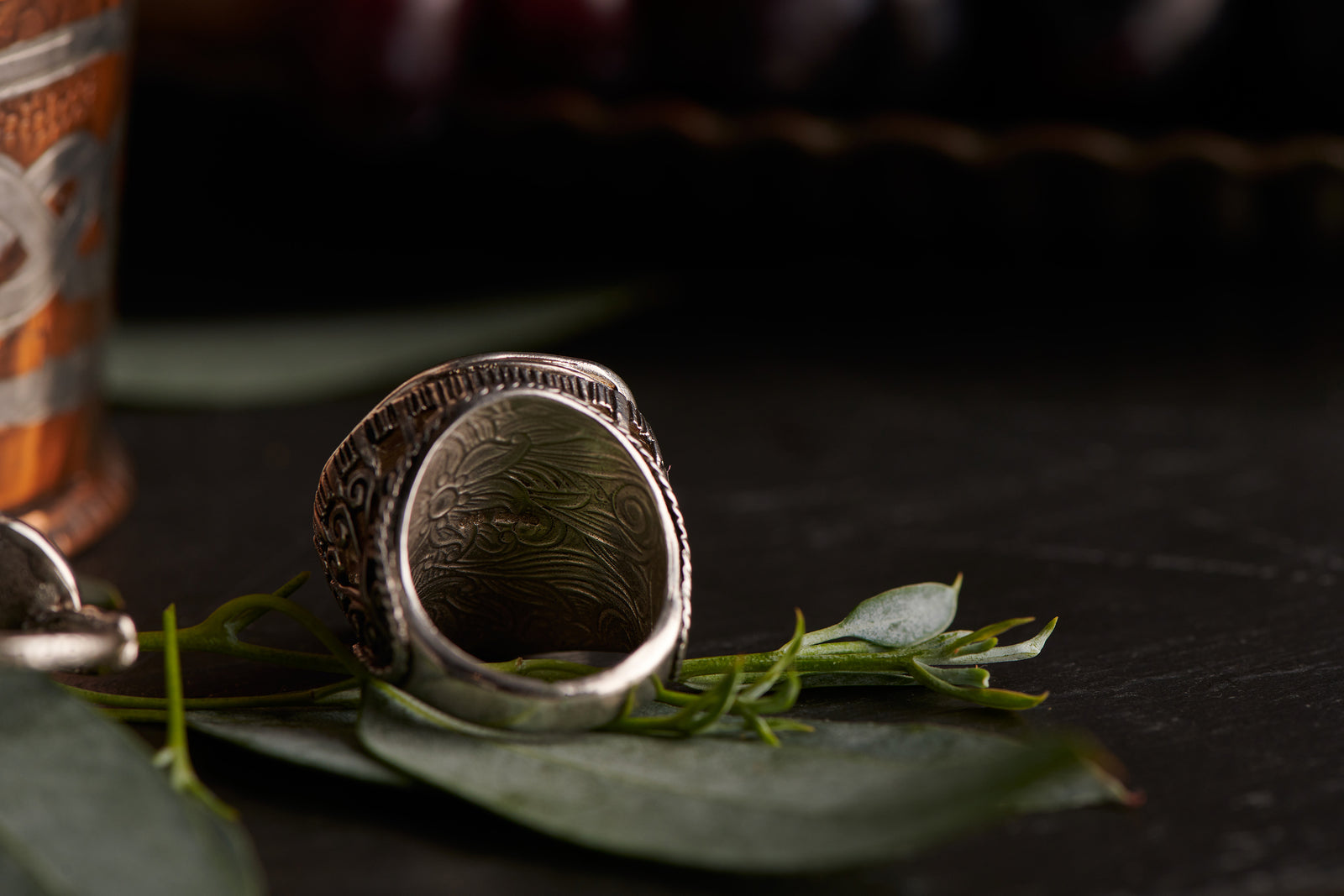 Silver ring with intricate design on a dark surface with leaves