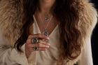 A woman with long brown hair, wearing a light blouse and fur stole, displays Jessica de Lotz Jewellery’s House of the Dragon & JdL Daemon Targaryen Wax Seal Sovereign Ring. The focus is on her jewelry and clothing; her face is mostly out of frame.