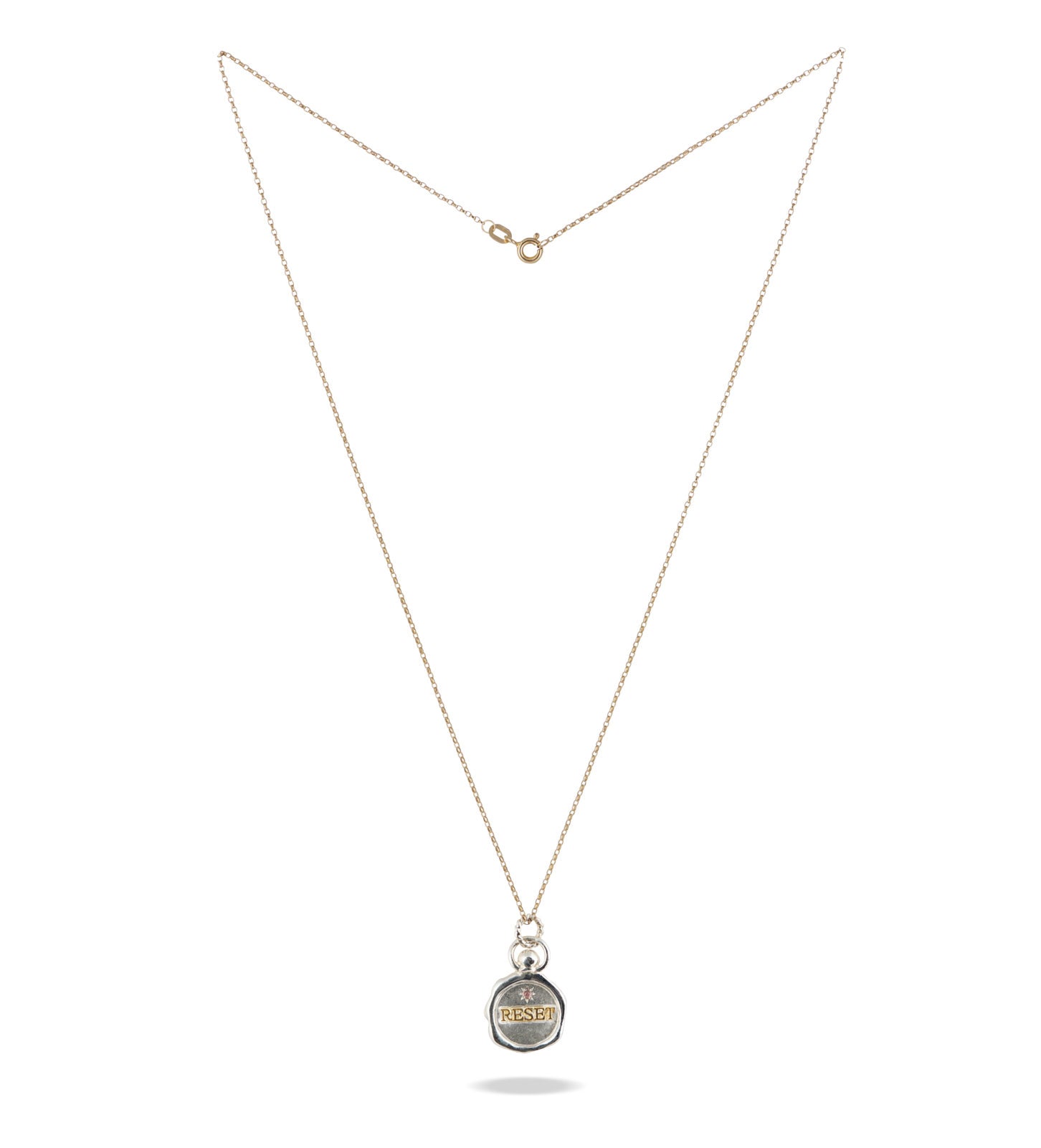 The RESET charm by Jessica de Lotz Jewellery features a delicate gold chain and a small round silver pendant engraved with “RESET.” Displayed on a white background, it symbolizes new beginnings—an ideal accessory for fresh starts.