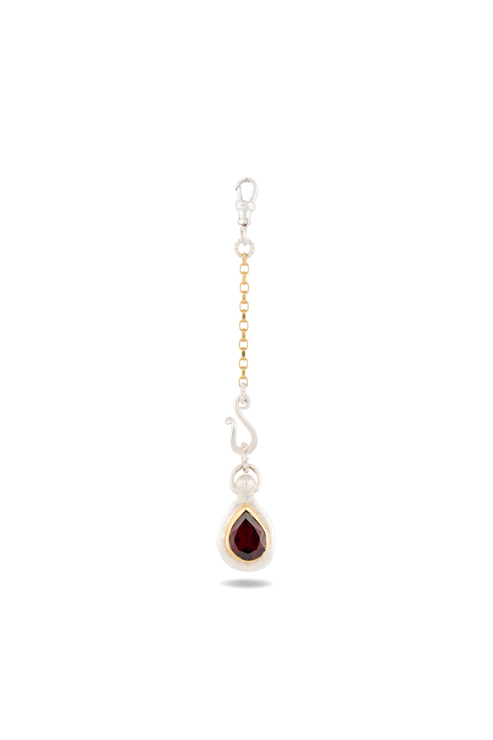 Introducing the “My Blood, Your Blood, Our Blood Charm” by Jessica de Lotz Jewellery—a single earring that features interwoven gold and silver chains, a decorative silver hook, and a teardrop-shaped red gemstone set in polished silver. Inspired by sisterhood jewelry from the Practical Magic charms collection, this standout piece is showcased against a plain white background, drawing attention to its intricate craftsmanship and striking colors.