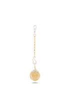 Introducing the “Midnight Margarita Lime Charm” by Jessica de Lotz Jewellery: This keychain features a gold circular pendant reminiscent of a lime slice, suspended from a short gold chain and finished with a silver lobster clasp. Perched atop the pendant is a small, abstract silver figure that provides striking contrast to the gold elements—capturing the spirit of modern-day chatelaine style. Set against a crisp white background.