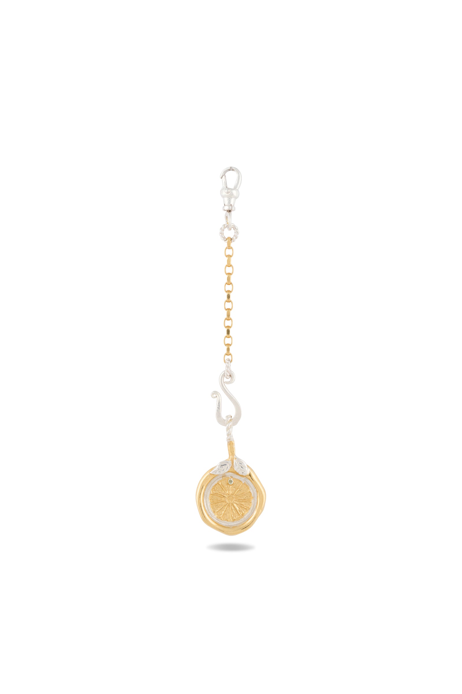 Introducing the “Midnight Margarita Lime Charm” by Jessica de Lotz Jewellery: This keychain features a gold circular pendant reminiscent of a lime slice, suspended from a short gold chain and finished with a silver lobster clasp. Perched atop the pendant is a small, abstract silver figure that provides striking contrast to the gold elements—capturing the spirit of modern-day chatelaine style. Set against a crisp white background.