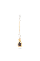 The “My Blood, Your Blood, Our Blood Charm” earring by Jessica de Lotz Jewellery features gold and silver chain accents with a teardrop-shaped red gemstone set in gold, topped with a decorative gold cap and finished with a small silver hook. Displayed against a plain white background, this unique piece is inspired by Practical Magic charms and beautifully captures the essence of sisterhood jewelry.