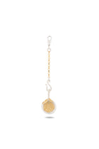 The Midnight Margarita Lime Charm by Jessica de Lotz Jewellery features a round, vibrant green dried lime slice encased in a clear circular frame, suspended from a gold chain with a silver lobster clasp and adorned with a decorative silver swirl. Reminiscent of Practical Magic charms and ideal for modern-day chatelaines, this unique accessory adds a touch of kitchen witchcraft to your everyday essentials. The background is plain white.