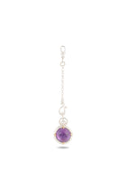 The ’There’s A Little Witch In All Of Us’ Charm by Jessica de Lotz Jewellery showcases a round, polished amethyst cabochon secured in a delicate wire cage and suspended from a fine silver chain with small links and a clasp at the top. Reminiscent of a modern-day chatelaine, the gemstone charm hangs gracefully at the bottom, set against a plain white background.