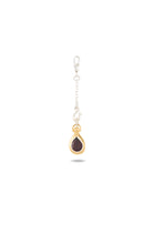 The “My Blood, Your Blood, Our Blood Charm” by Jessica de Lotz Jewellery features a single silver chain earring with a gold-framed, teardrop-shaped dark gemstone pendant and a sleek silver clasp. Shown against a plain white background, this striking piece of sisterhood jewelry is inspired by the magical charms of Practical Magic.