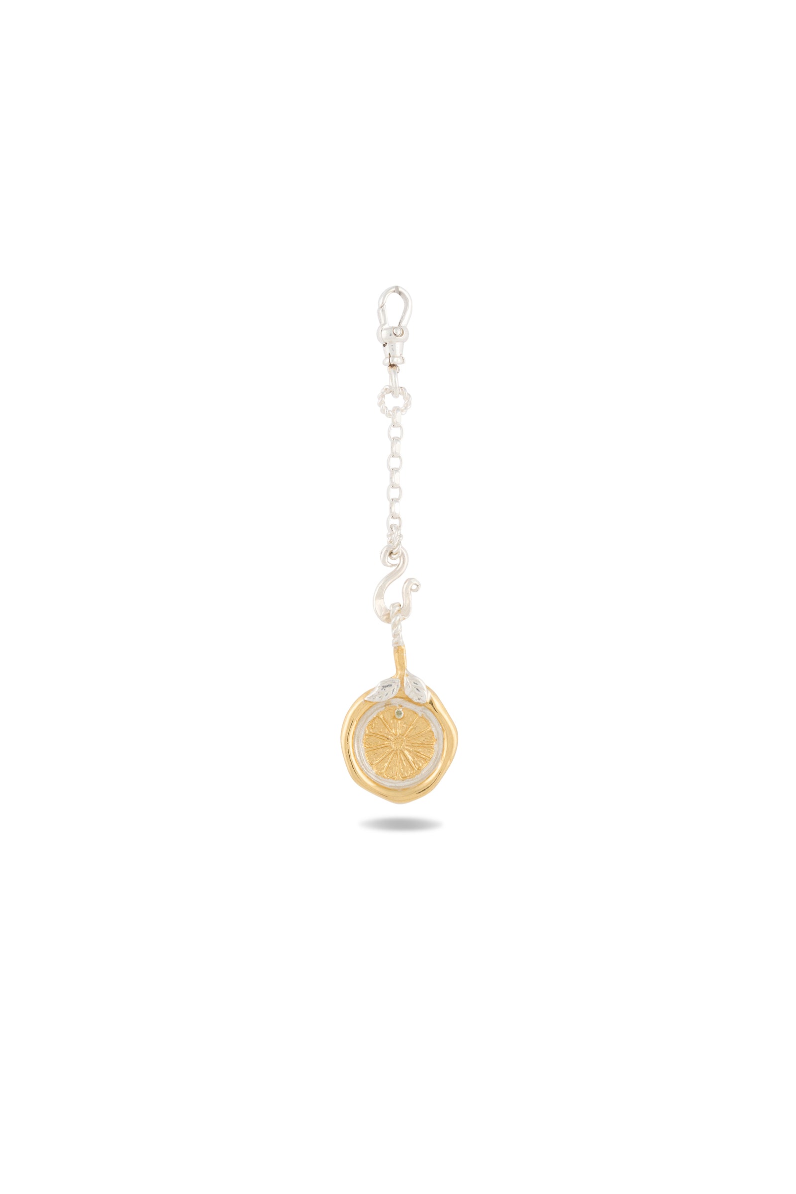 A silver keychain with a short chain and clasp holds Jessica de Lotz Jewellery’s Midnight Margarita Lime Charm—a round, gold-tone medallion adorned with a stylized sunburst design. Reminiscent of modern-day chatelaine accessories, this piece channels the spirit of Practical Magic charms as the medallion dangles from the end of the chain, casting a delicate shadow on a white background.