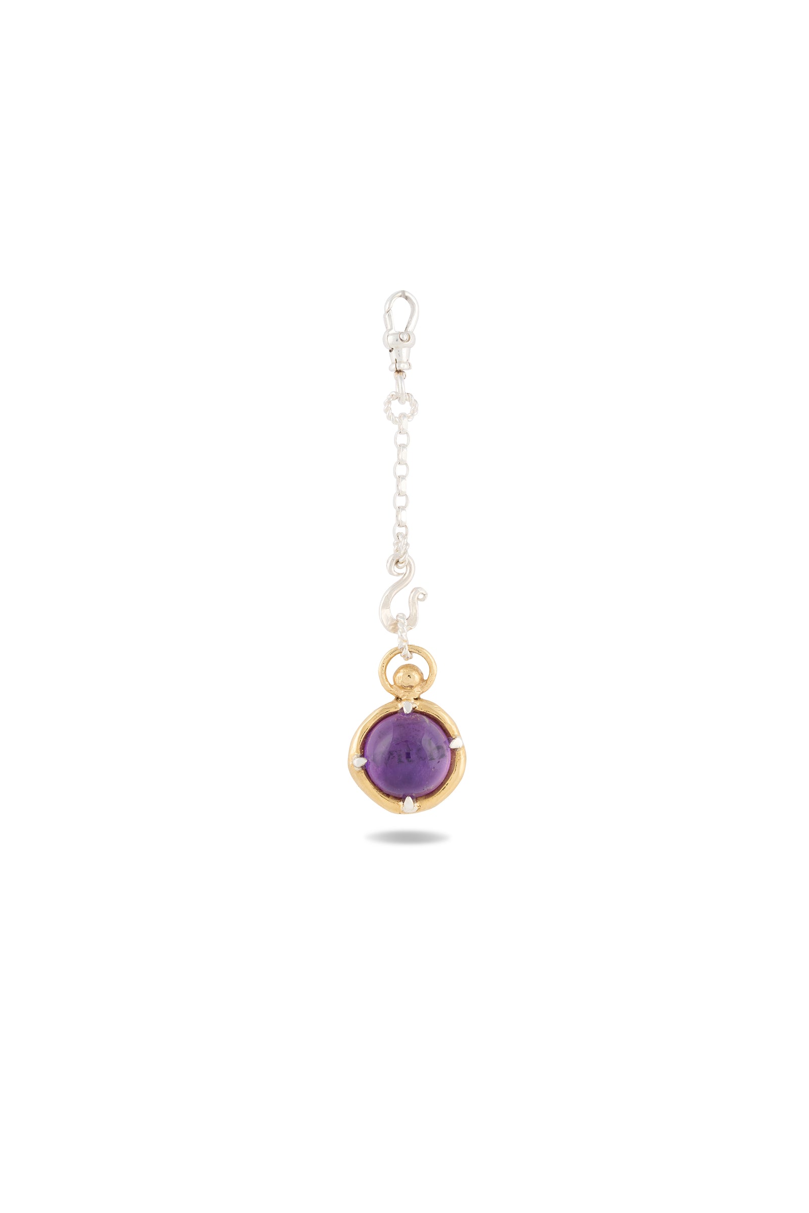 A single earring from Jessica de Lotz Jewellery, the ’There’s A Little Witch In All Of Us’ Charm, features a delicate silver chain adorned with small white bead accents and a round amethyst cabochon set in a gold bezel at the end. Presented on a white background with a faint shadow beneath, it offers a subtle nod to Practical Magic charms for the modern-day chatelaine.