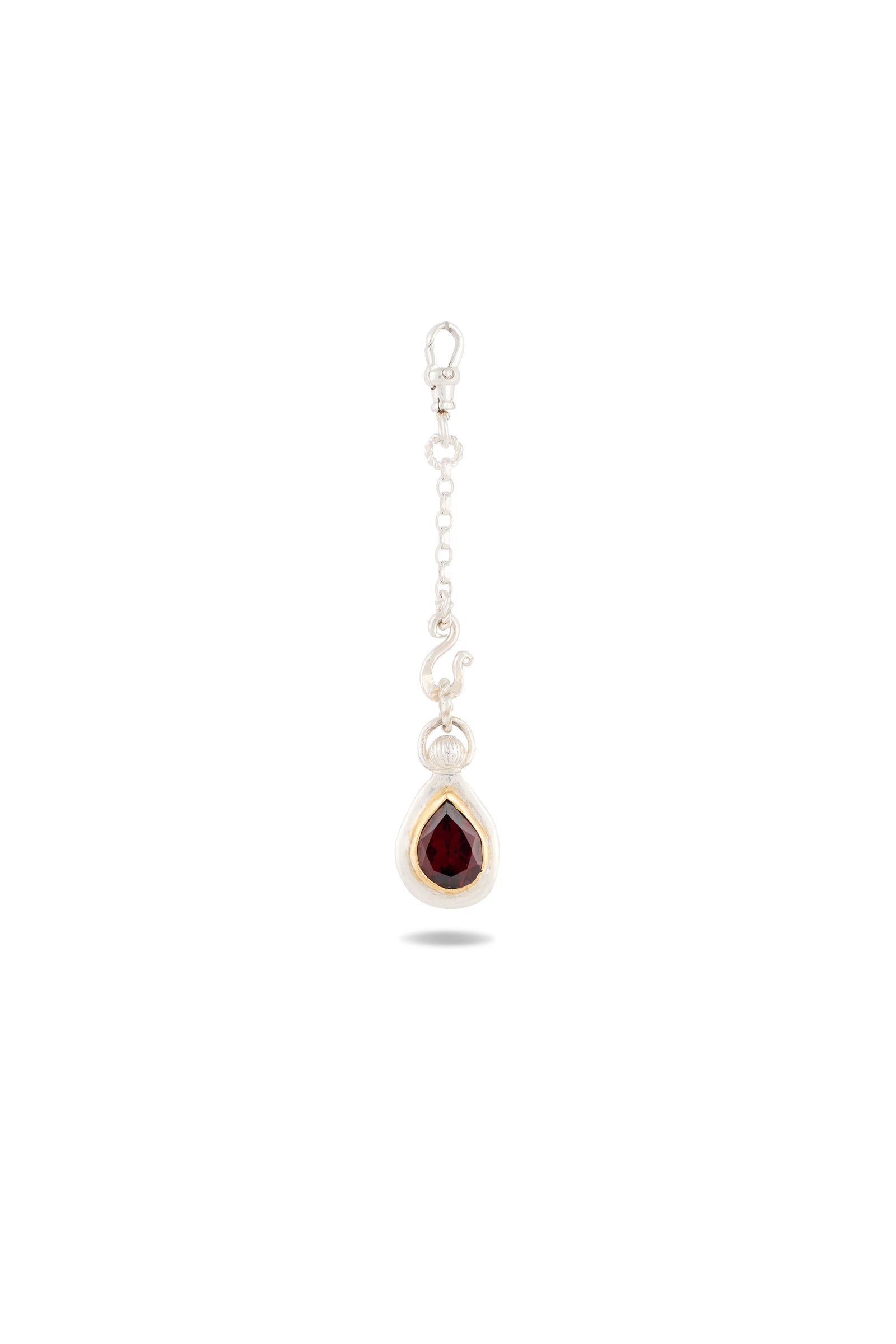 A silver earring with a delicate chain and hook, featuring a teardrop-shaped deep red gemstone set in a silver bezel—this elegant piece, the “My Blood, Your Blood, Our Blood Charm” by Jessica de Lotz Jewellery, draws inspiration from sisterhood jewelry and evokes the mystical bonds reminiscent of Practical Magic charms. The background is plain white with a faint shadow beneath the earring.