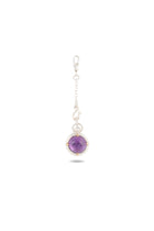 A delicate silver keychain from Jessica de Lotz Jewellery, the ’There’s A Little Witch In All Of Us’ Charm, features a round amethyst cabochon encased in a silver setting. Reminiscent of a modern-day chatelaine, the keychain is designed with a lobster clasp and a short chain of small decorative links, displayed on a plain white background with a faint shadow beneath.