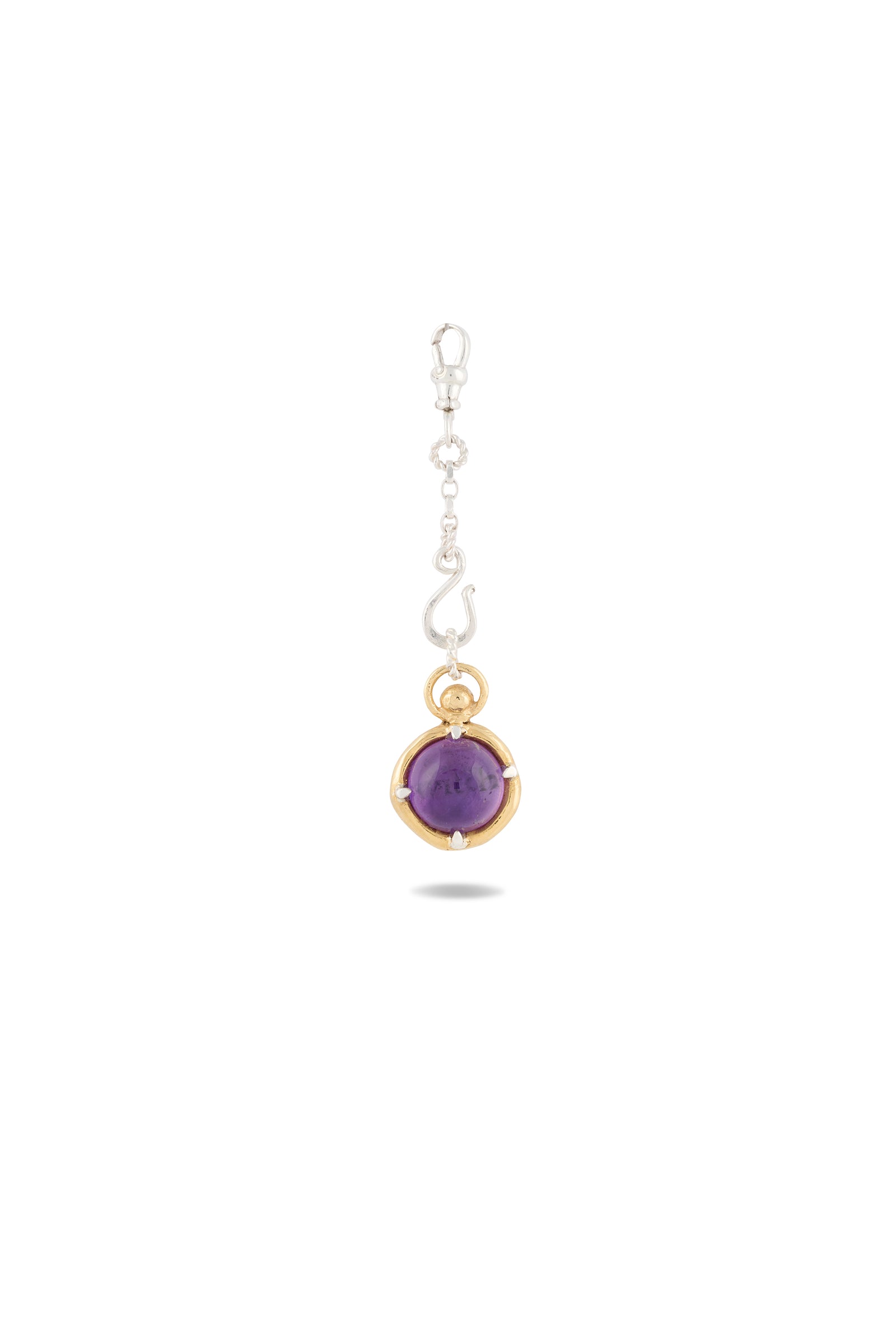 A dangling pendant earring from Jessica de Lotz Jewellery, the ’There’s A Little Witch In All Of Us’ Charm features a silver hook and chain, with a round amethyst cabochon set in a smooth gold bezel at the bottom. Shown against a white background, the vibrant purple stone and mixed-metal design evoke whimsical Practical Magic charms, while the earring casts a subtle shadow beneath.