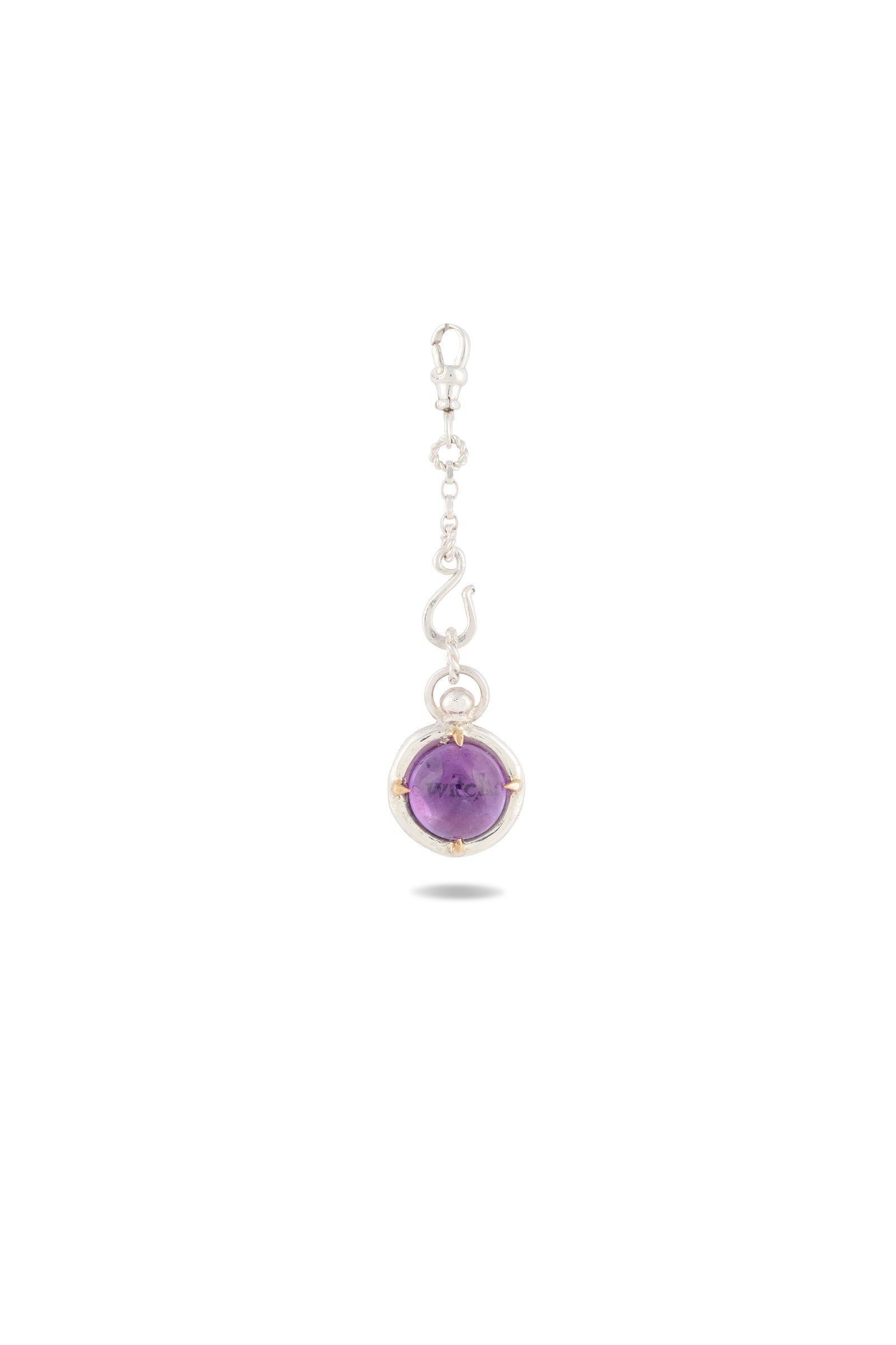 A silver dangle earring from Jessica de Lotz Jewellery, the ’There’s A Little Witch In All Of Us’ Charm, features a hook top, an elegant decorative swirl, and a glossy round amethyst cabochon set within a circular silver frame. Reminiscent of Practical Magic charms for the modern-day chatelaine, the gemstone is securely held by four slender prongs. The piece is photographed on a plain white background with a subtle shadow beneath.