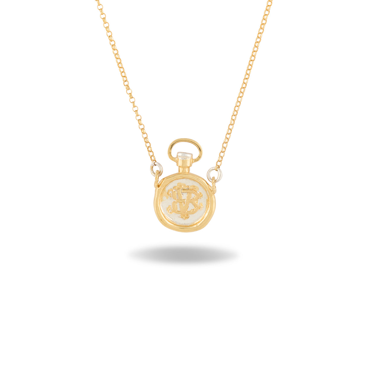 A delicate gold necklace by Jessica de Lotz Jewellery, the Verbenca Botanical Charm Apothecary Top, features a small pendant inspired by a classic apothecary stopper, intricately engraved with ornate initials. Reminiscent of Practical Magic jewelry, the chain is thin and fine, and the pendant casts a soft shadow on a white background.