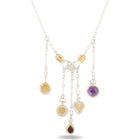 The Practical Magic Chatelaine Holding Hands Necklace (Charm & Chain Bundle) by Jessica de Lotz Jewellery features a silver design with gold accents and a central handshake charm, inspired by the brand’s iconic style. Five dangling pendants—a circular engraved disc, a heart, an amethyst circle, a round gold-accented medallion, and a teardrop-shaped garnet stone—grace the chain, evoking the enchanting spirit of Practical Magic. Displayed on a white background.
