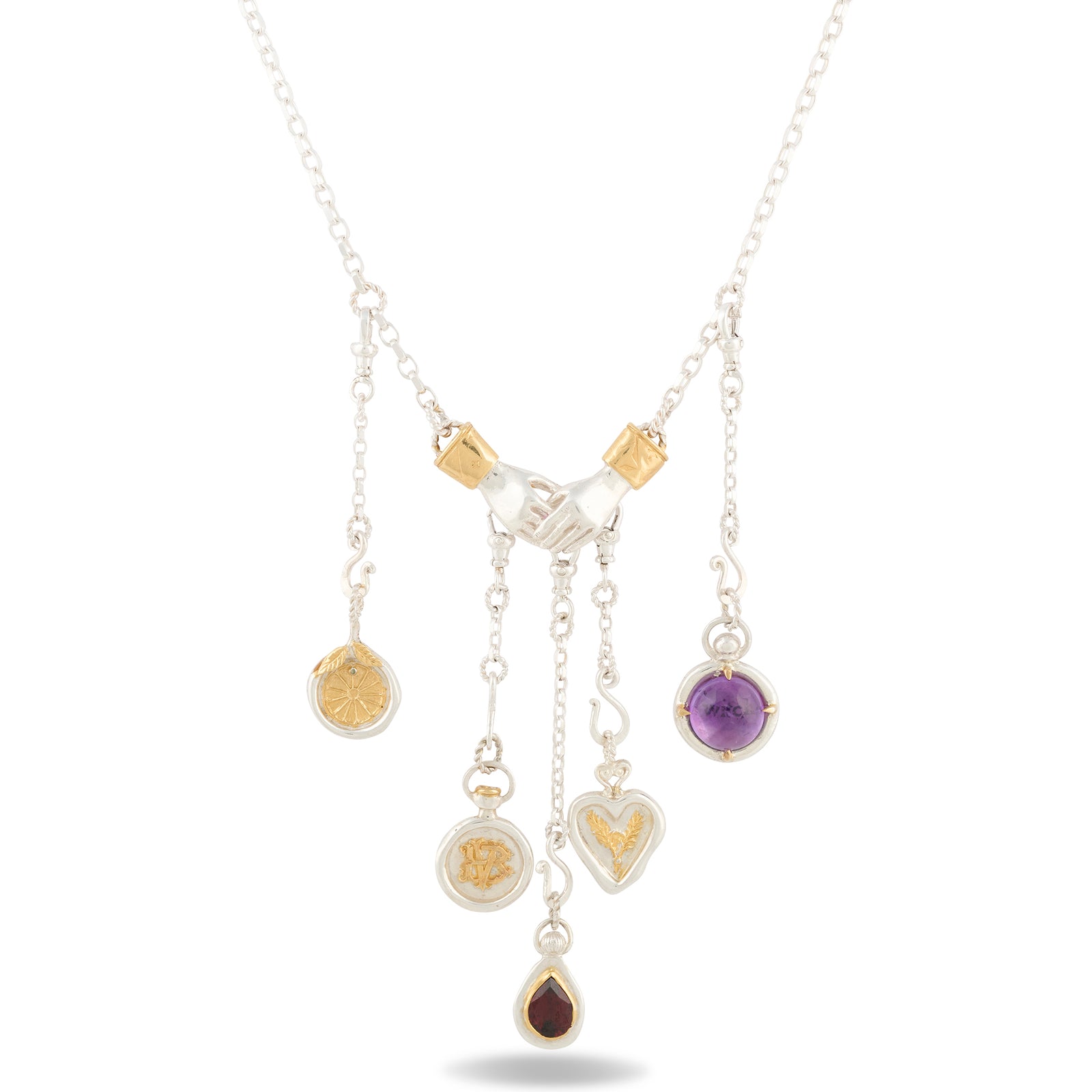 The Practical Magic Chatelaine Holding Hands Necklace (Charm & Chain Bundle) by Jessica de Lotz Jewellery features a silver design with gold accents and a central handshake charm, inspired by the brand’s iconic style. Five dangling pendants—a circular engraved disc, a heart, an amethyst circle, a round gold-accented medallion, and a teardrop-shaped garnet stone—grace the chain, evoking the enchanting spirit of Practical Magic. Displayed on a white background.