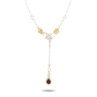 The Chatelaine Hand Necklace with ‘Our Blood’ Drop Charm by Jessica de Lotz Jewellery features two silver clasped hands with gold cuffs, joined by a delicate chain. Suspended below is a vertical drop ending in a teardrop-shaped, dark red gemstone framed in silver—evoking the mystical aesthetic of Practical Magic. Set against a plain white background, the pendant casts a subtle shadow.