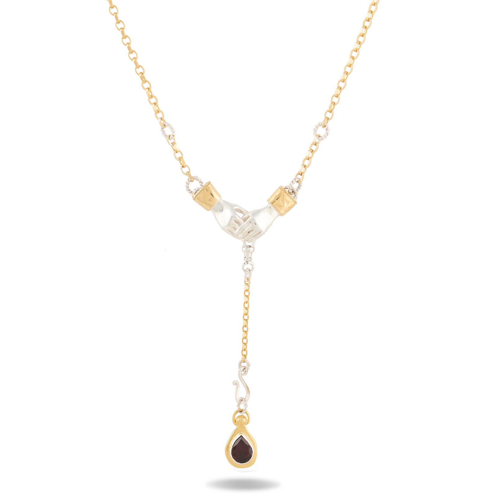 The Chatelaine Hand Necklace with ‘Our Blood’ Drop Charm by Jessica de Lotz Jewellery features two hands clasped at the center, accented with a teardrop-shaped red gemstone and small round white stones along the chain. This delicate piece mixes gold and silver tones in a symmetrical design, evoking vintage charm reminiscent of Practical Magic 2 charms.