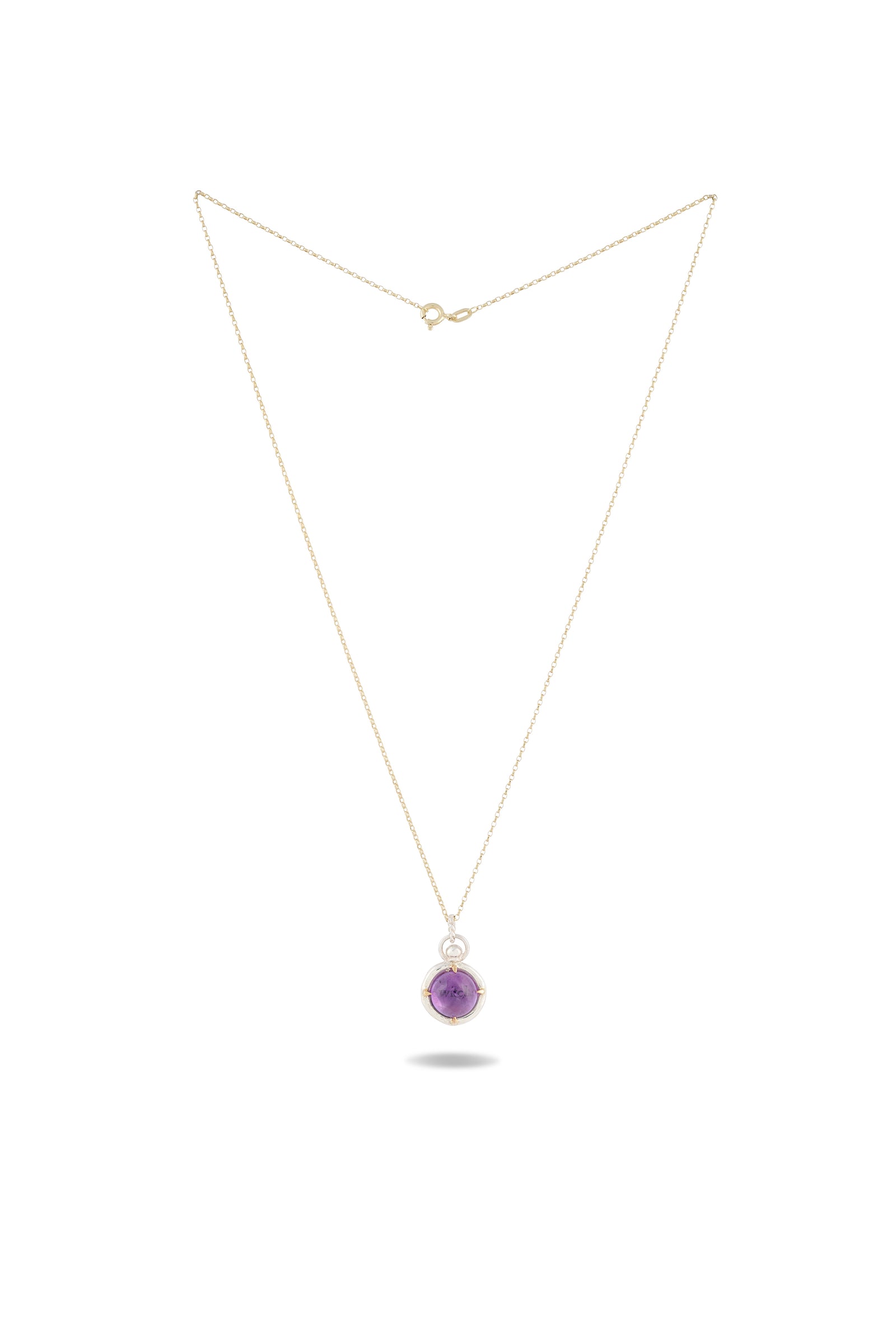 A delicate gold chain necklace featuring the ’There’s A Little Witch In All Of Us’ charm by Jessica de Lotz Jewellery, displayed against a white background. The round amethyst cabochon pendant hangs centrally and casts a faint shadow below, highlighting its simple and elegant design reminiscent of a modern-day chatelaine.