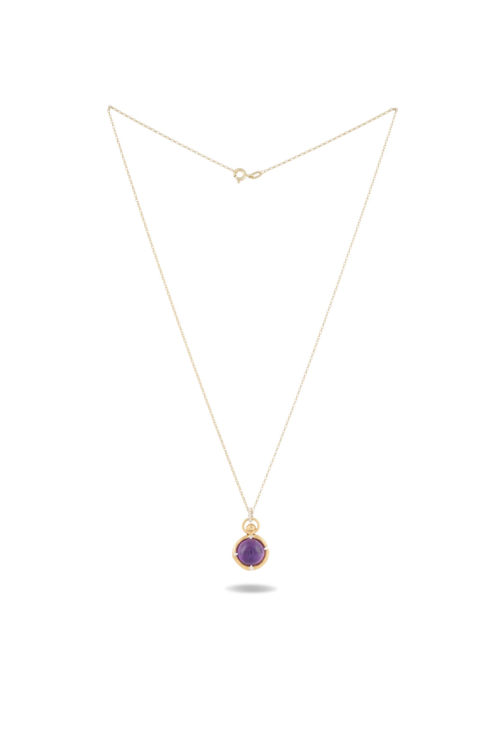 A delicate gold chain necklace by Jessica de Lotz Jewellery features the ’There’s A Little Witch In All Of Us’ charm, a round amethyst cabochon pendant in a gold setting inspired by modern-day chatelaine style, shown against a white background with a small shadow beneath the pendant.