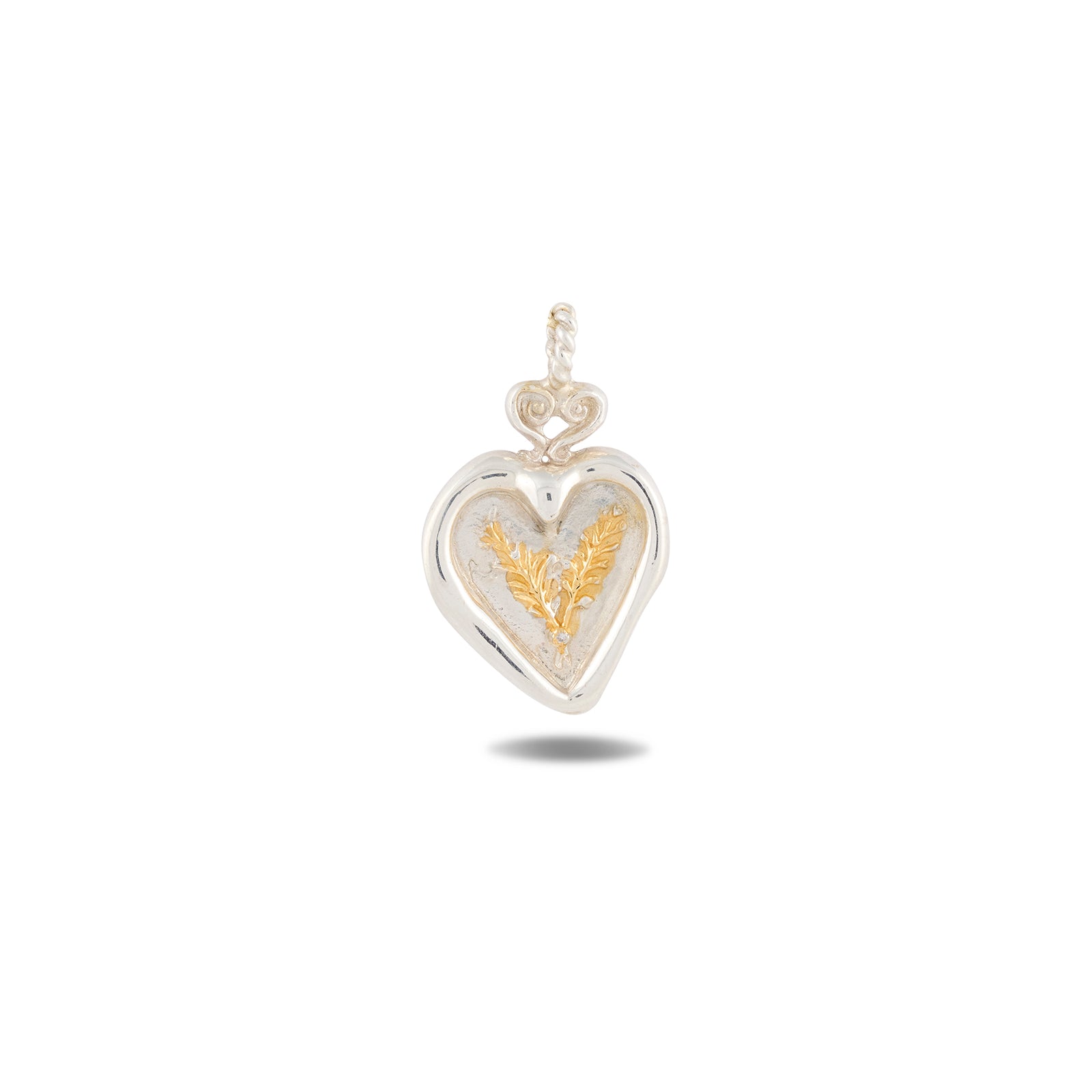 Certainly! Here’s a rewritten sentence using the provided product data: The Amas Veritas Charm by Jessica de Lotz Jewellery features a silver heart-shaped pendant with a twisted loop at the top, capturing an enchanting aesthetic. At its center lies an intricate gold fern design, evoking the whimsical allure of Practical Magic charms. The pendant is showcased against a white background with a faint shadow below.