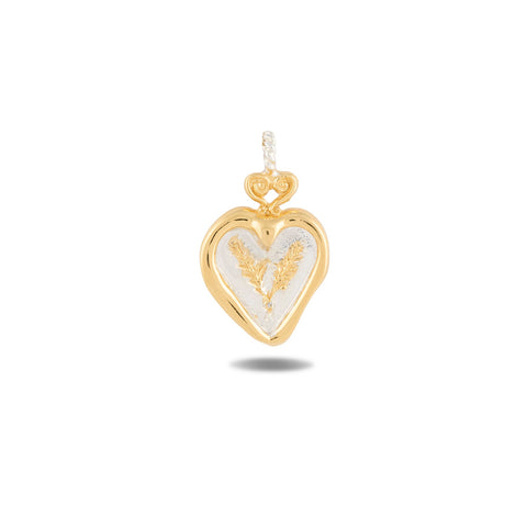 The Amas Veritas Charm by Jessica de Lotz Jewellery is a heart-shaped pendant in gold and silver, featuring a loop at the top for hanging. Its center showcases a textured, intricate design inspired by Practical Magic charms, and the pendant casts a subtle shadow on a white background.