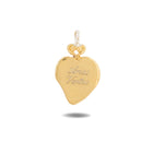 A gleaming gold heart-shaped pendant, the Amas Veritas Charm by Jessica de Lotz Jewellery, features a delicate loop at the top for attaching to a chain. Inspired by Practical Magic charms, it is engraved with the words “Amor Veritas.” A subtle shadow appears beneath the pendant against a plain white background.