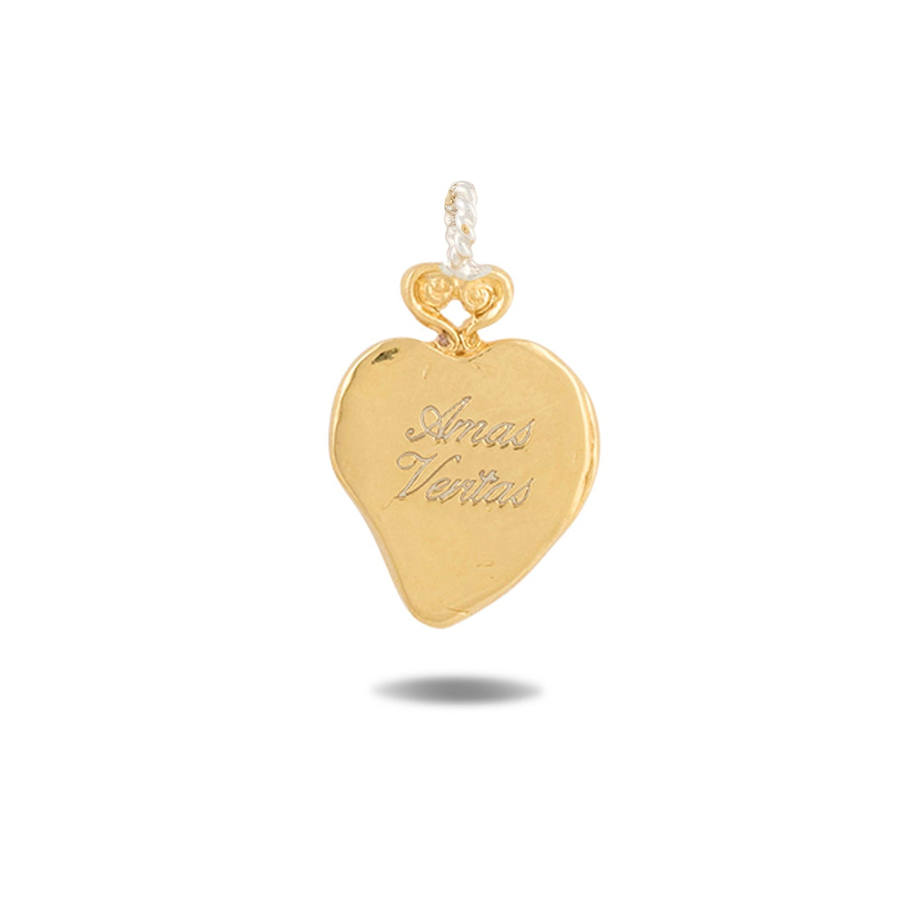 A gleaming gold heart-shaped pendant, the Amas Veritas Charm by Jessica de Lotz Jewellery, features a delicate loop at the top for attaching to a chain. Inspired by Practical Magic charms, it is engraved with the words “Amor Veritas.” A subtle shadow appears beneath the pendant against a plain white background.