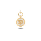 A petite, round gold pendant—Jessica de Lotz Jewellery’s Verbenca Botanical Charm Bottle Top—displays a white-centered design adorned with an ornate monogram or symbol at its core, echoing the brand’s iconic Practical Magic aesthetics. The pendant features a circular loop at the top for effortless attachment to a chain and casts a gentle shadow on a white background.