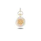 A small, round silver Verbenca Botanical Charm Bottle Top by Jessica de Lotz Jewellery features a twisted loop at the top. Reminiscent of Practical Magic charms, its center displays an ornate gold monogram with the letters V and B intertwined. The pendant casts a faint shadow on the white background.