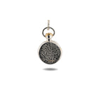 The Verbenca Botanical Charm Bottle Top by Jessica de Lotz Jewellery is a petite, round silver pendant inspired by vintage wax seal charms. Its face features a textured black botanical motif, and it hangs from a twisted silver loop accented with gold at the top. The charm is photographed against a plain white background, casting a gentle shadow below.