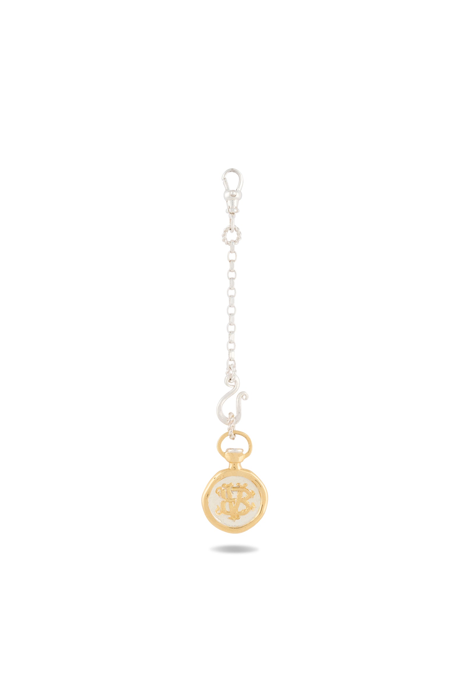 A gold, round “Verbena Botanical Apothecary Bottle Charm” by Jessica de Lotz Jewellery hangs from a short silver chain with a lobster clasp at the top. Featuring an engraved design inspired by botanical wax-seal charm styles, this unique piece evokes the allure of sisterhood jewelry and Practical Magic charms. Set against a pure white background, the charm casts a faint shadow below.