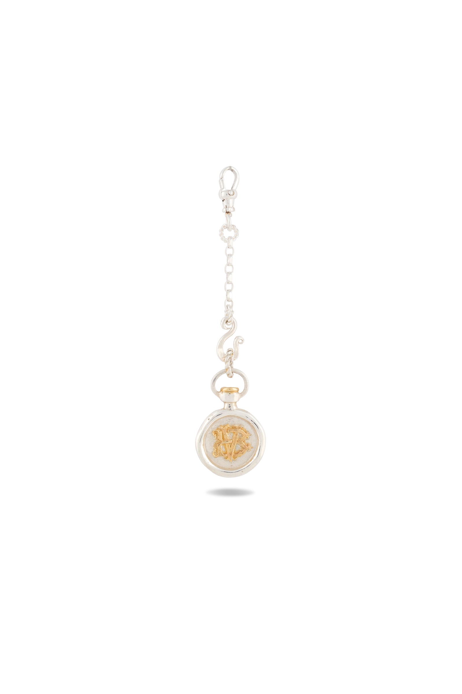 A Verbena Botanical Apothecary Bottle Charm by Jessica de Lotz Jewellery, featuring a gold-tone round pendant with an ornate relief design, is suspended from a short decorative silver chain with a clasp. Reminiscent of sisterhood jewelry and imbued with the enchanting essence of Practical Magic-inspired charms, this piece is beautifully showcased against a white background, its delicate shadow cast beneath it.