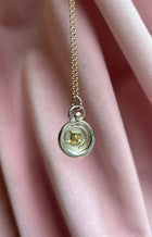 The Mini Personalised Wax Seal Charms by JdL Jewellery feature a gold chain necklace with a circular initial R charm, set against a metallic background and displayed on soft pink fabric for an elegant touch.