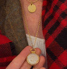 A close-up of a person wearing a gold personalised necklace engraved with "Mummy" and a date, plus the Jessica de Lotz Jewellery Large Double Sealed Wax Seal Necklace with a large circular pendant held in their hand.