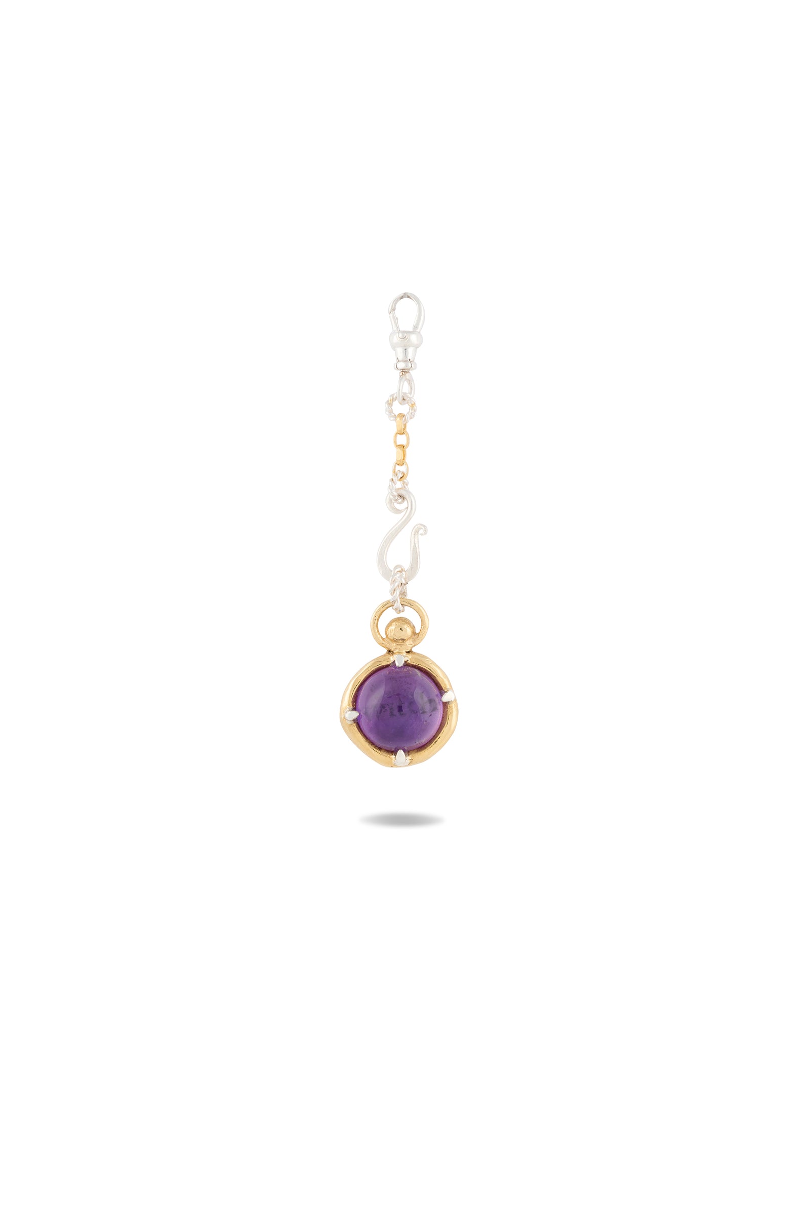 The ’There’s A Little Witch In All Of Us’ Charm by Jessica de Lotz Jewellery features a round amethyst cabochon set in a gold bezel and is attached to a silver chain adorned with small gold accents. Inspired by modern-day chatelaine accessories, the charm casts a faint shadow below on a white background.