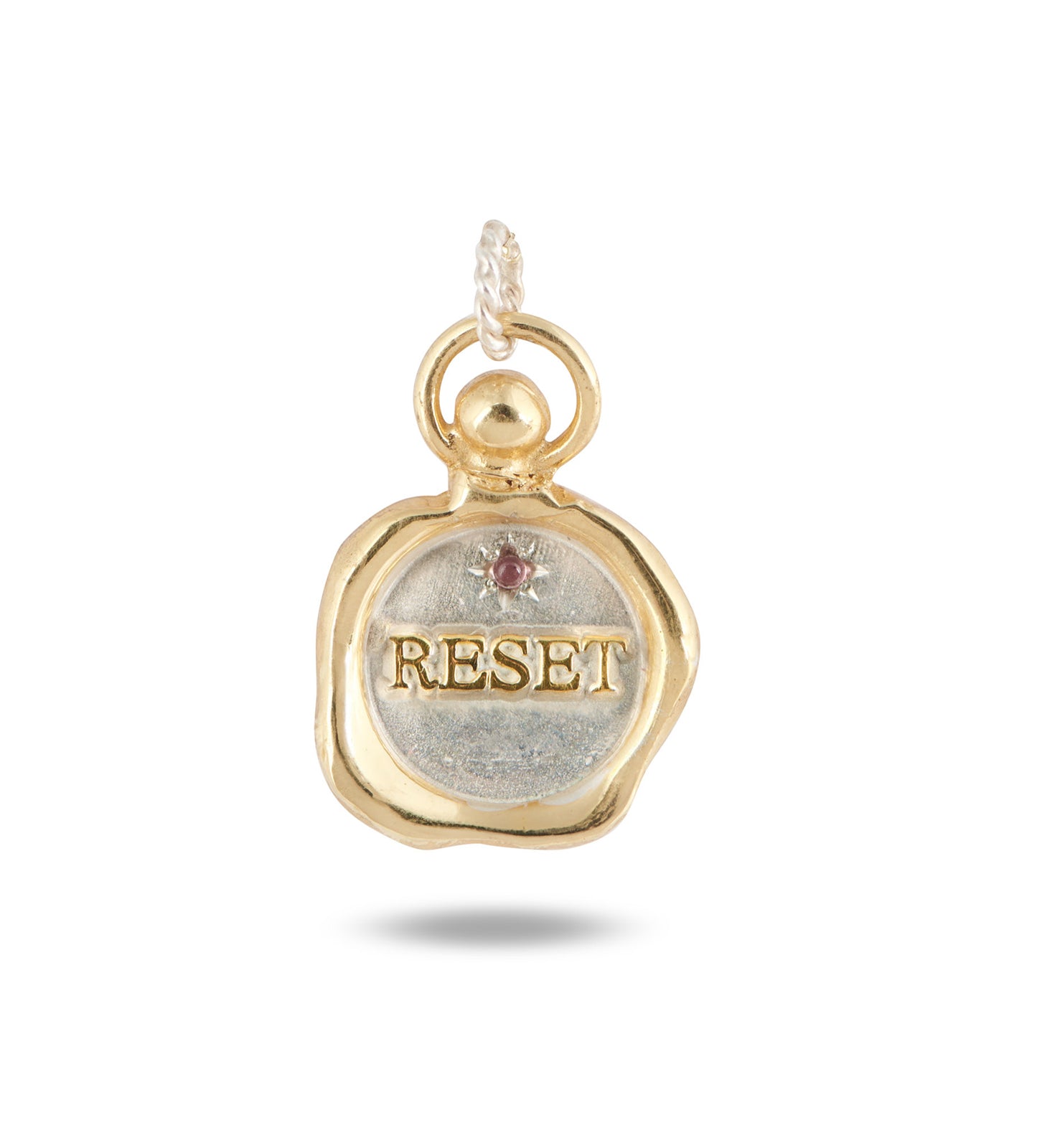 The RESET charm by Jessica de Lotz Jewellery is a round gold and silver wax seal pendant with a raised gold border, "RESET" engraved in gold on silver, accented by a small pink tourmaline and clear gem, hanging from a twisted gold loop.