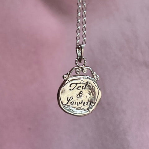 Silver necklace with a round pendant on a pink background