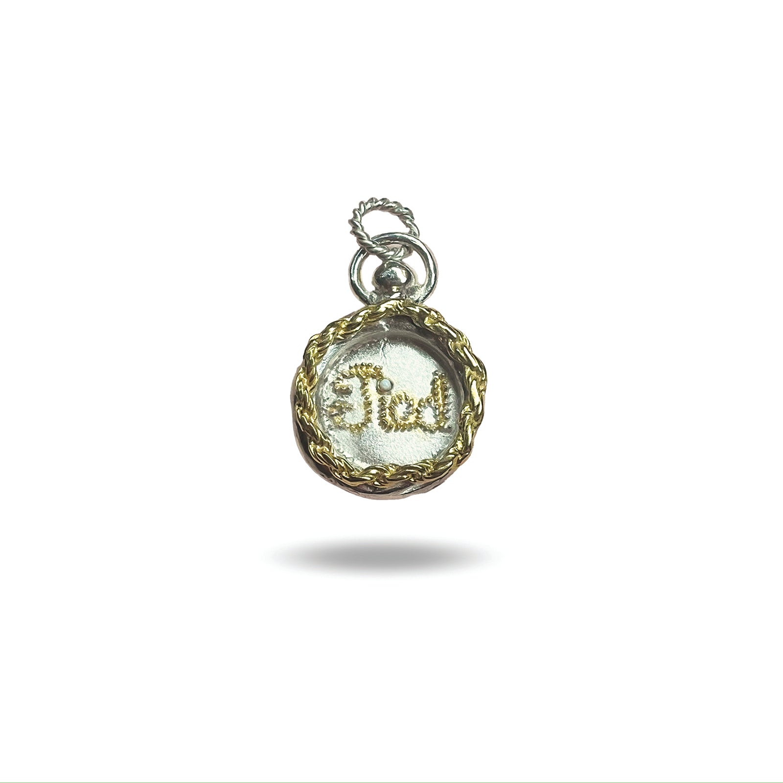 The Tied Charm by Jessica de Lotz Jewellery is a round silver pendant with a gold braided border and “God” in cursive, resembling a wax seal. It features a silver loop for attaching to a chain and is shown on a white background.