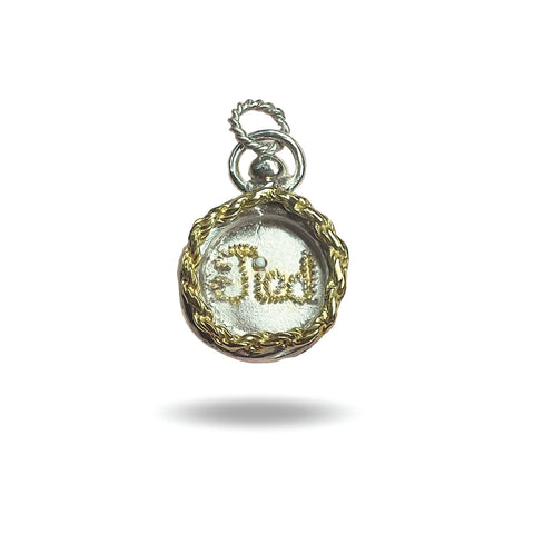 The Tied Charm by Jessica de Lotz Jewellery is a round silver pendant with a gold braided border and “God” in cursive, resembling a wax seal. It features a silver loop for attaching to a chain and is shown on a white background.