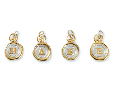 Personalise your JdL Jewellery with the Charm Add-On—four gold and silver wax seal-style charms, each with a raised letter (M, A, K, E), gold edges, and looped tops for easy attachment to your favourite necklace.